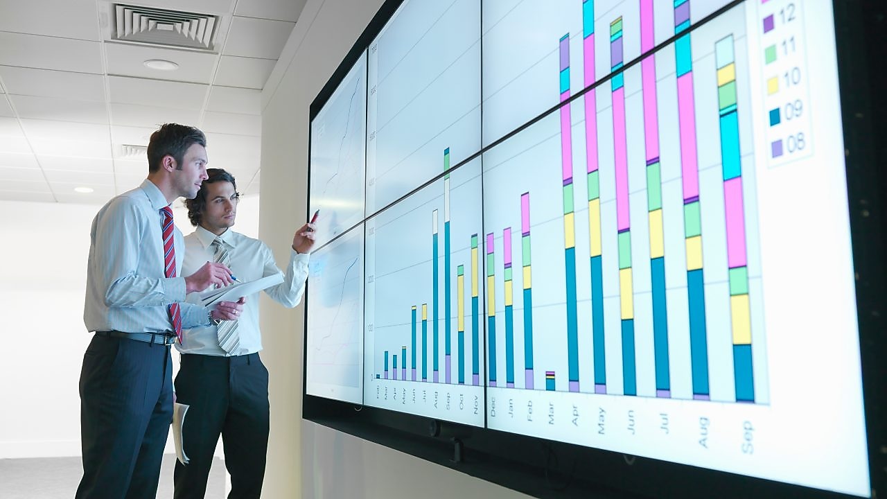 Бизнесмены анализируют данные отчетности, показанные на большом цифровом экране