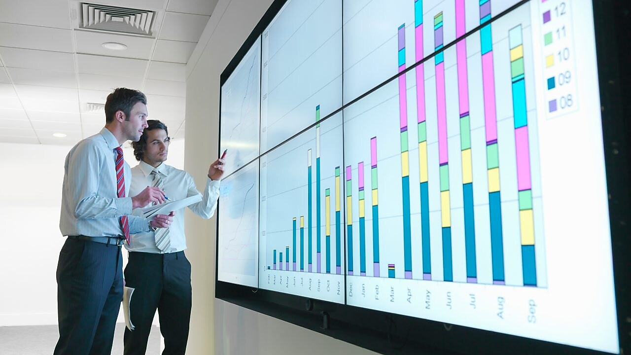 Бизнесмены анализируют данные отчетности, показанные на большом цифровом экране