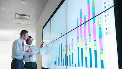 Бизнесмены анализируют данные отчетности, показанные на большом цифровом экране