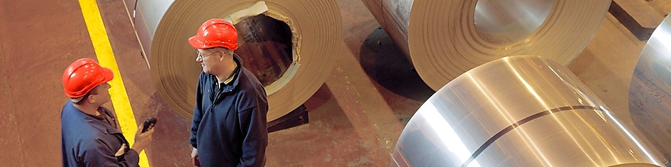 Два работника завода стоят рядом с тележкой расплавленной стали