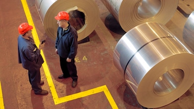 Два работника завода стоят рядом с тележкой расплавленной стали