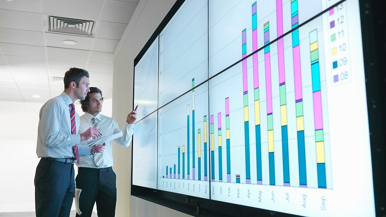 Бизнесмены анализируют данные отчетности, показанные на большом цифровом экране
