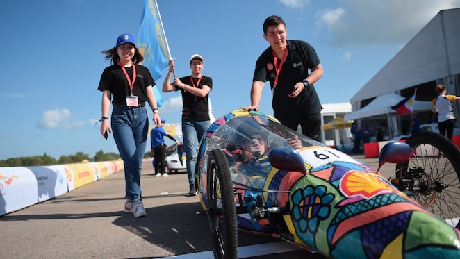 Студенты толкают прототип энергоэффективного автомобиля во время соревнований Shell Eco‑marathon; на корпусе автомобиля виден логотип Shell.